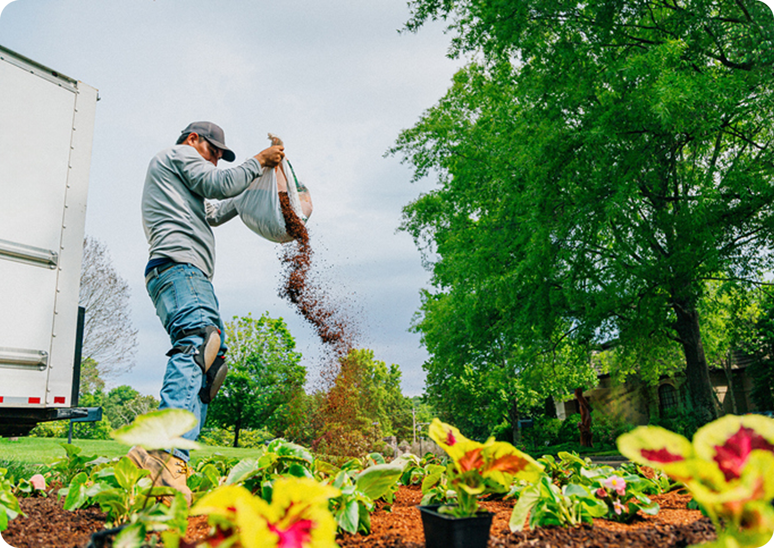 Gardener spreading mulch on flower bed.