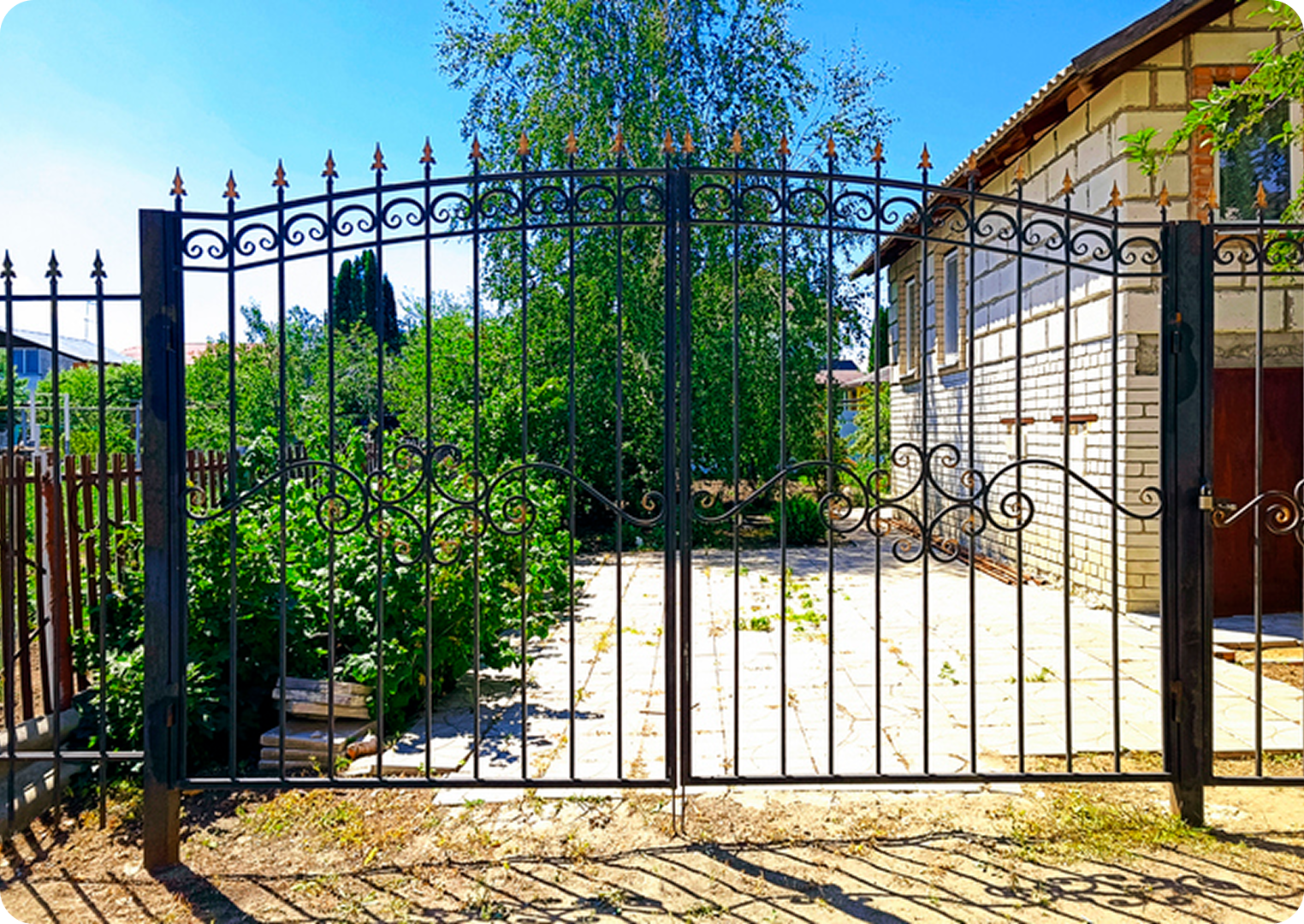 Ornate black gate with garden and house.