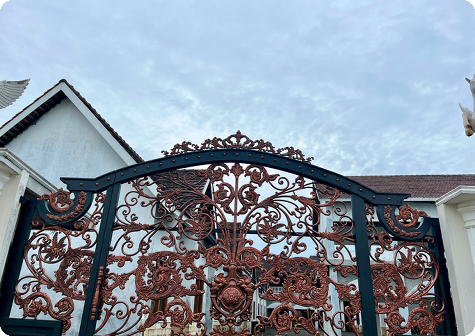 Ornate wrought iron gate against cloudy sky.