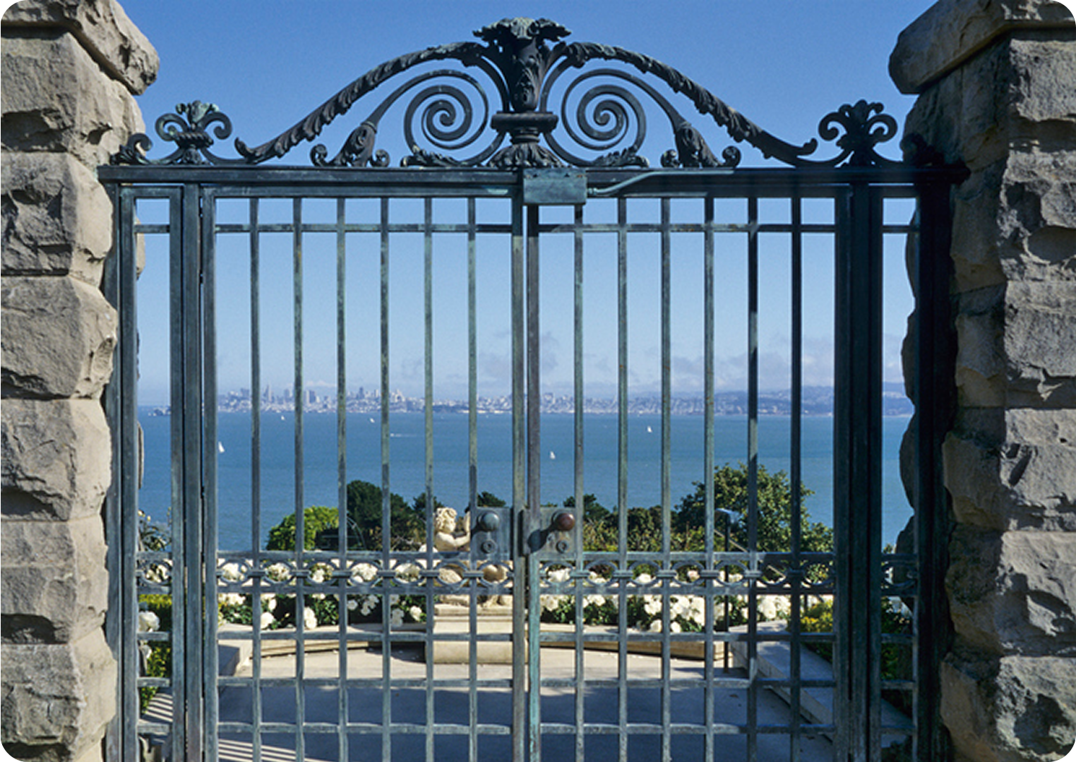Ornate gate overlooking ocean and city skyline.