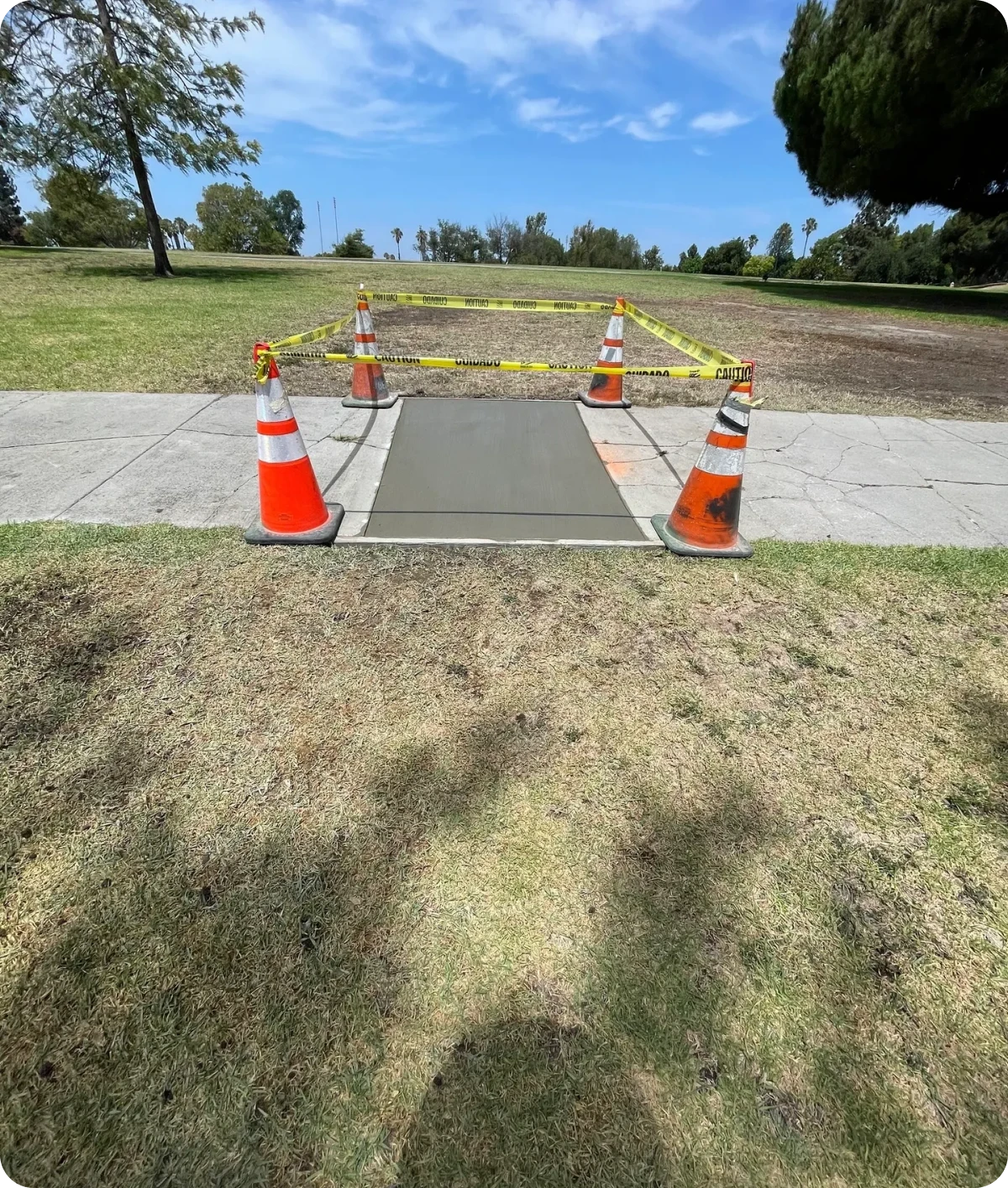 Wet cement sidewalk section with traffic cones.