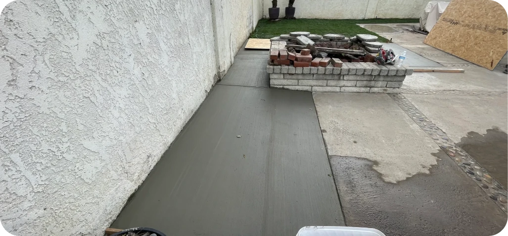 Freshly poured concrete slab near brick structure.