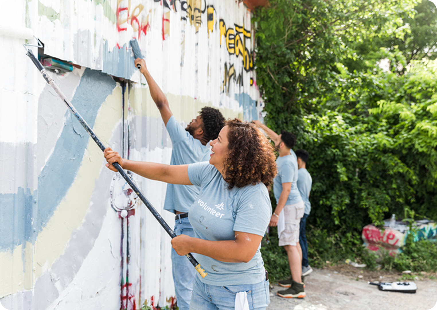 People painting over graffiti on wall.